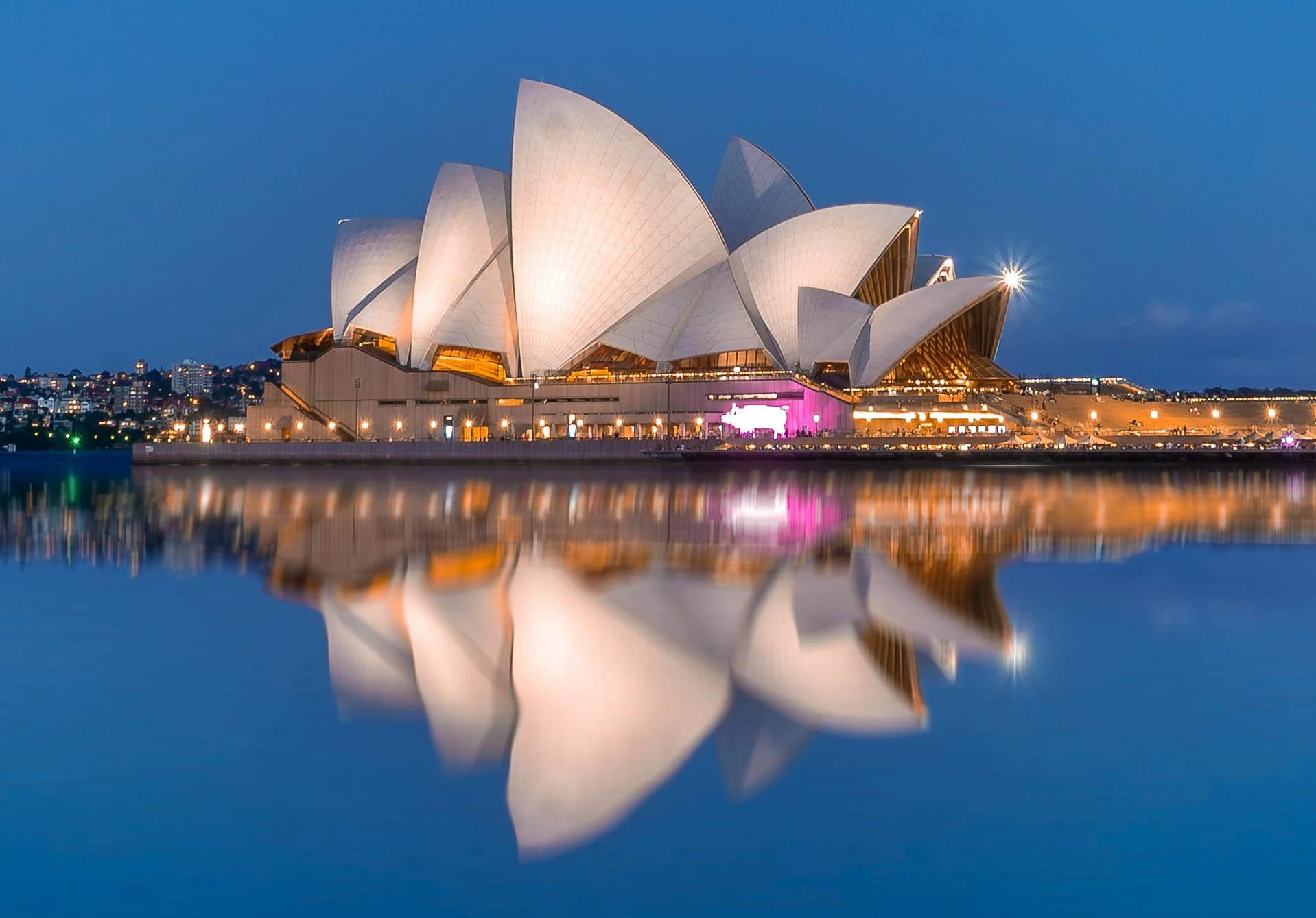 Sydney Opera House lit at dusk across the harbour
